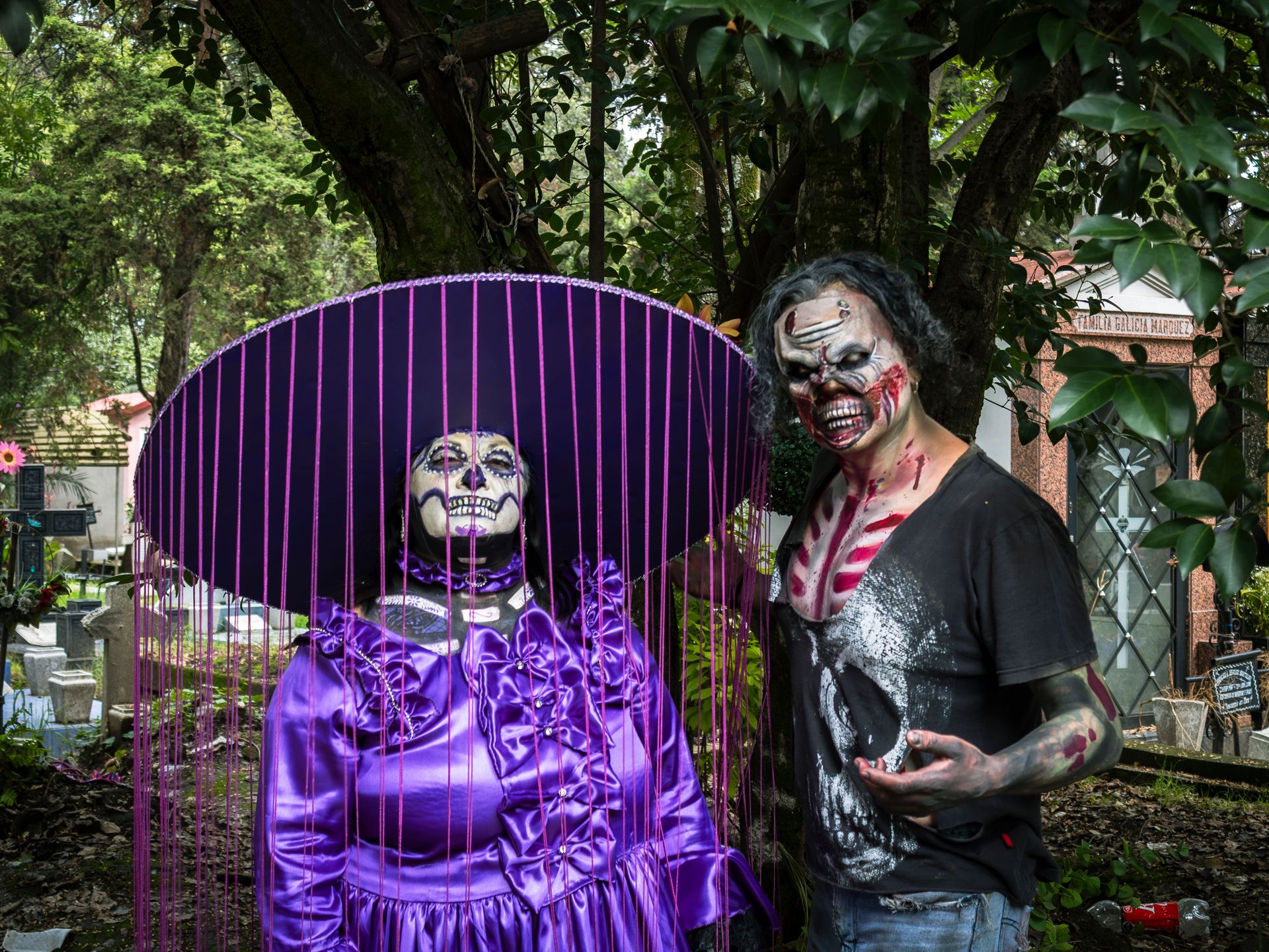 Two individuals in elaborate Halloween costumes posing outdoors with a spooky background.