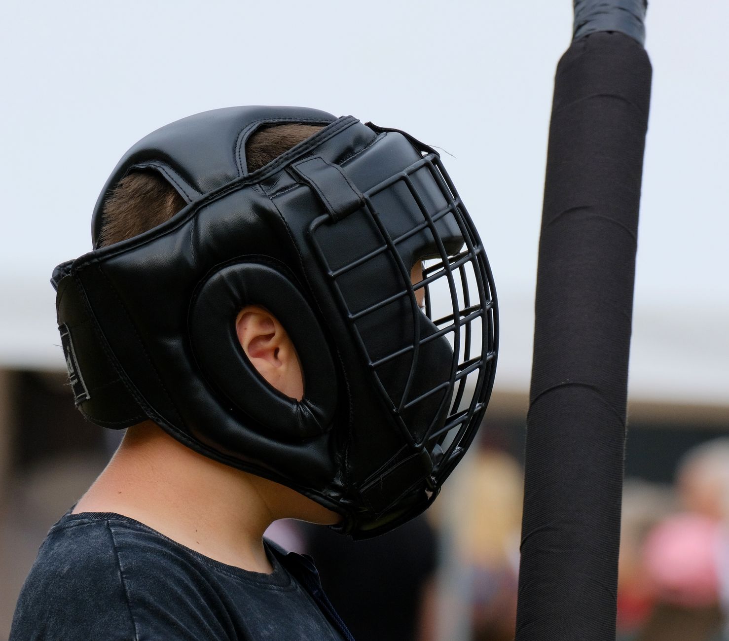 Outdoor scene of person in protective headgear with practice sword, ready for martial arts training.