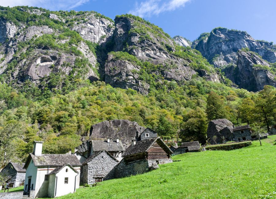 Charming stone houses nestled in a lush Swiss valley surrounded by towering cliffs.