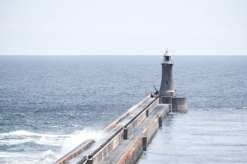 Free A serene view of a lighthouse guiding ships over the open sea with waves crashing on the jetty. Stock Photo