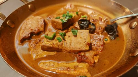 Close-up of braised tofu in a rich brown sauce with scallions and black mushrooms.