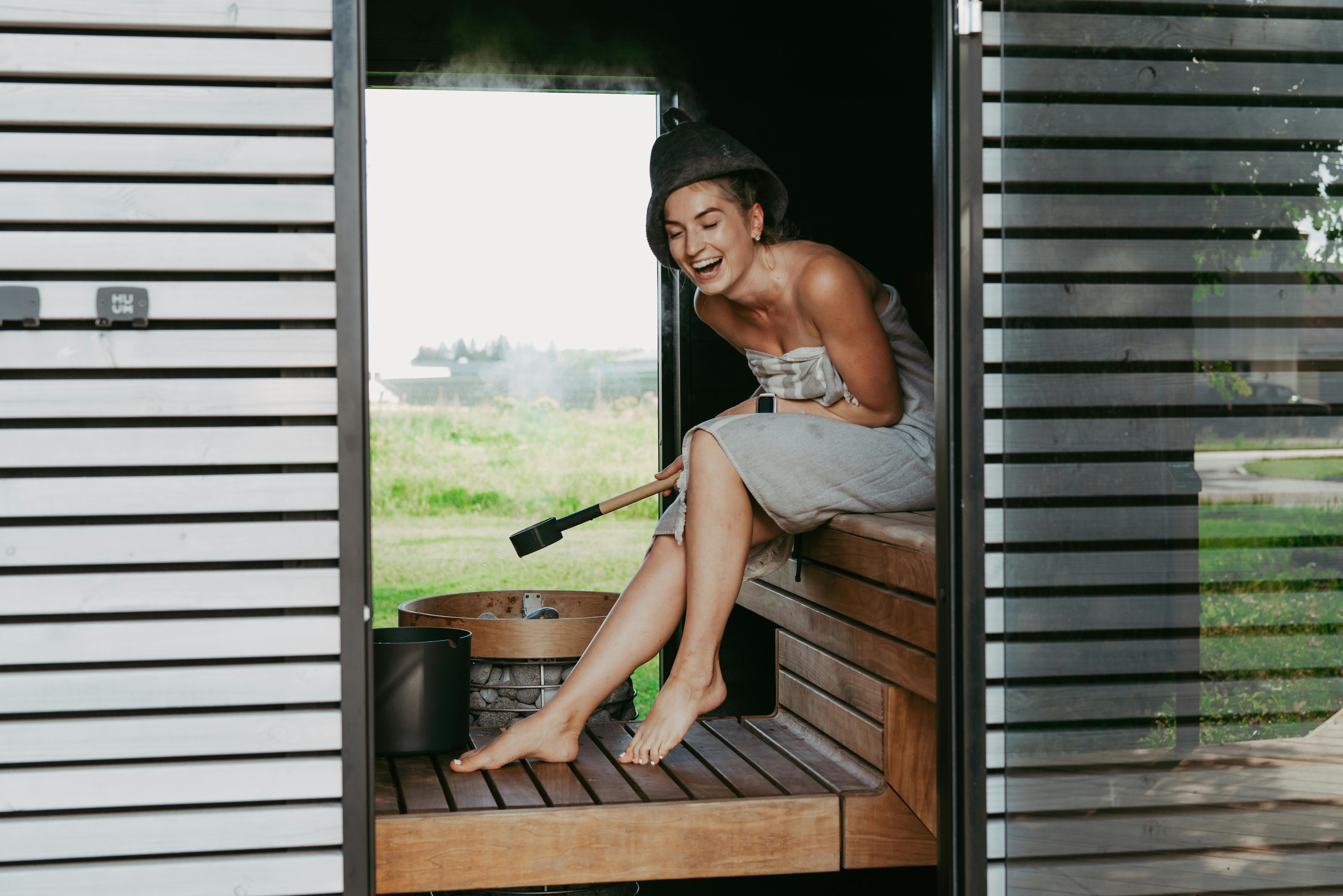 Woman relaxing in a modern sauna with warm wood panels and a serene outdoor view through large windows