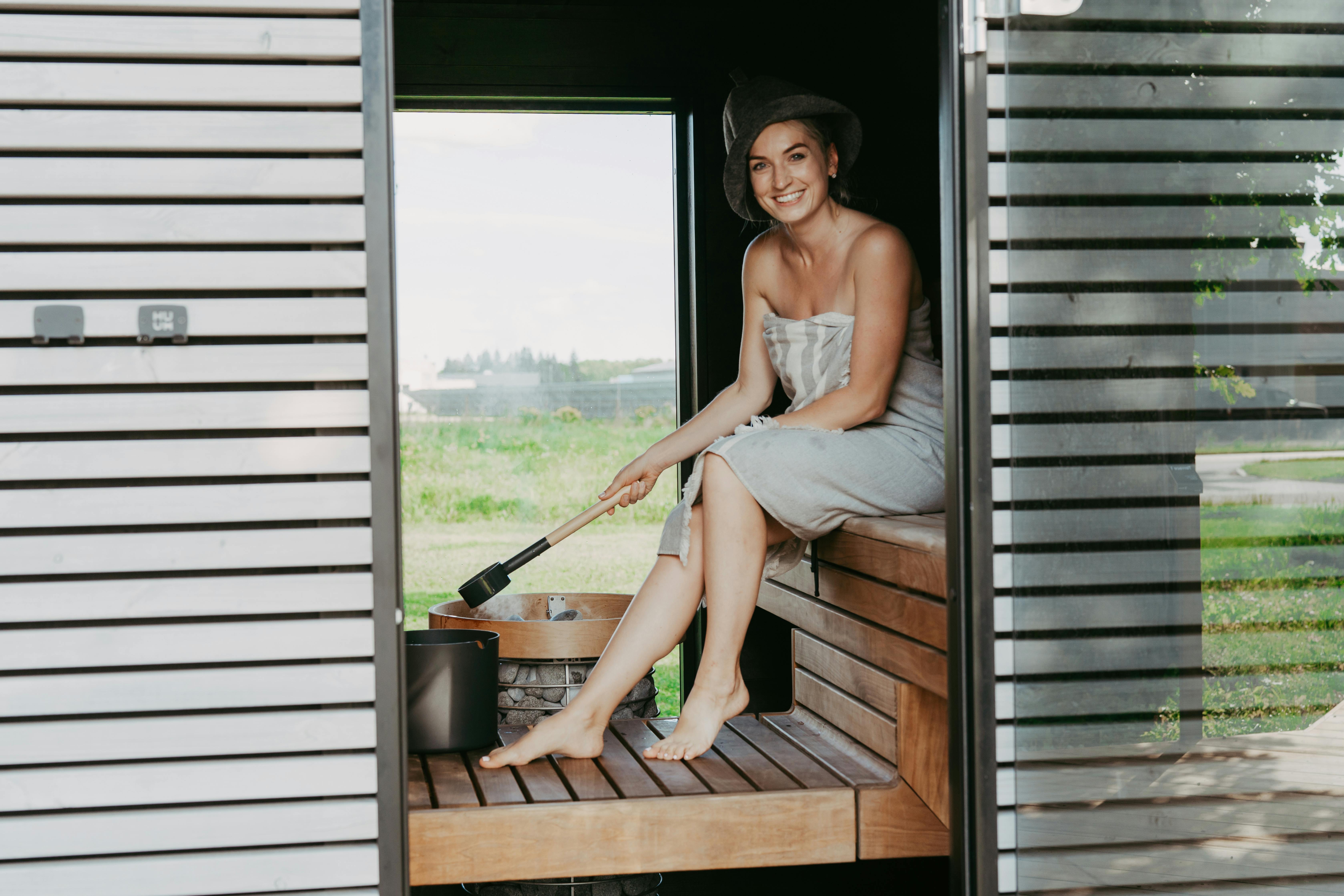 Une femme profite d'un moment de détente dans un sauna de style nordique, assise et souriante.