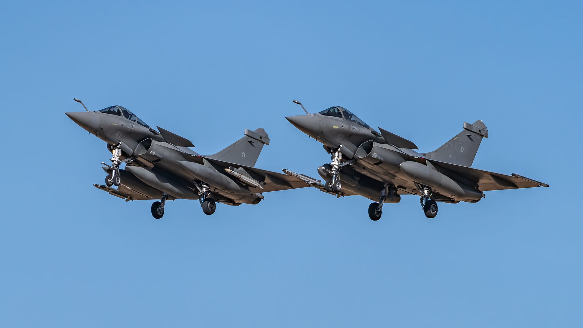 Two sleek Rafale fighter jets demonstrate airborne agility against a clear sky.