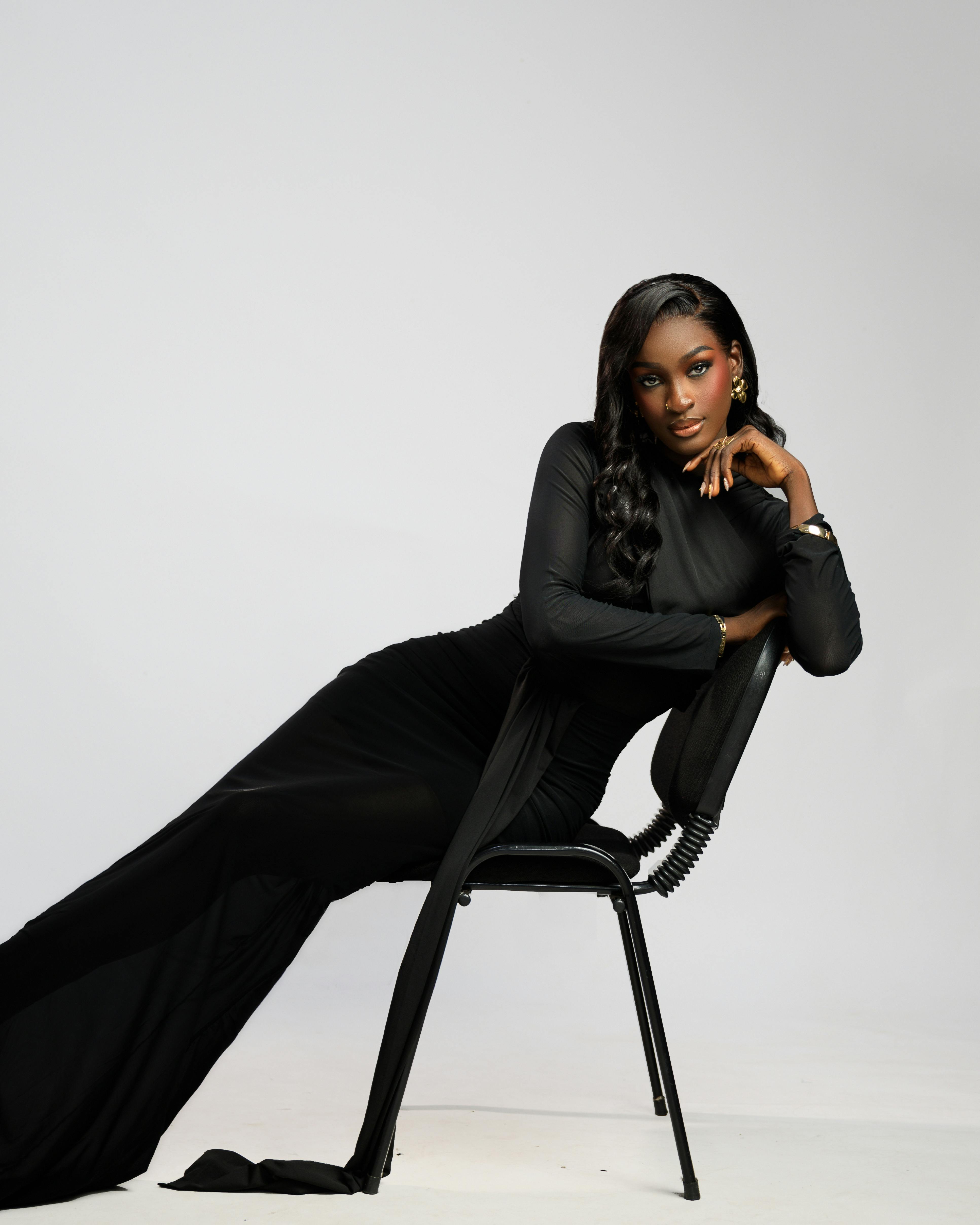 Fashion portrait of a stylish woman in a sleek black dress posed elegantly on a chair.