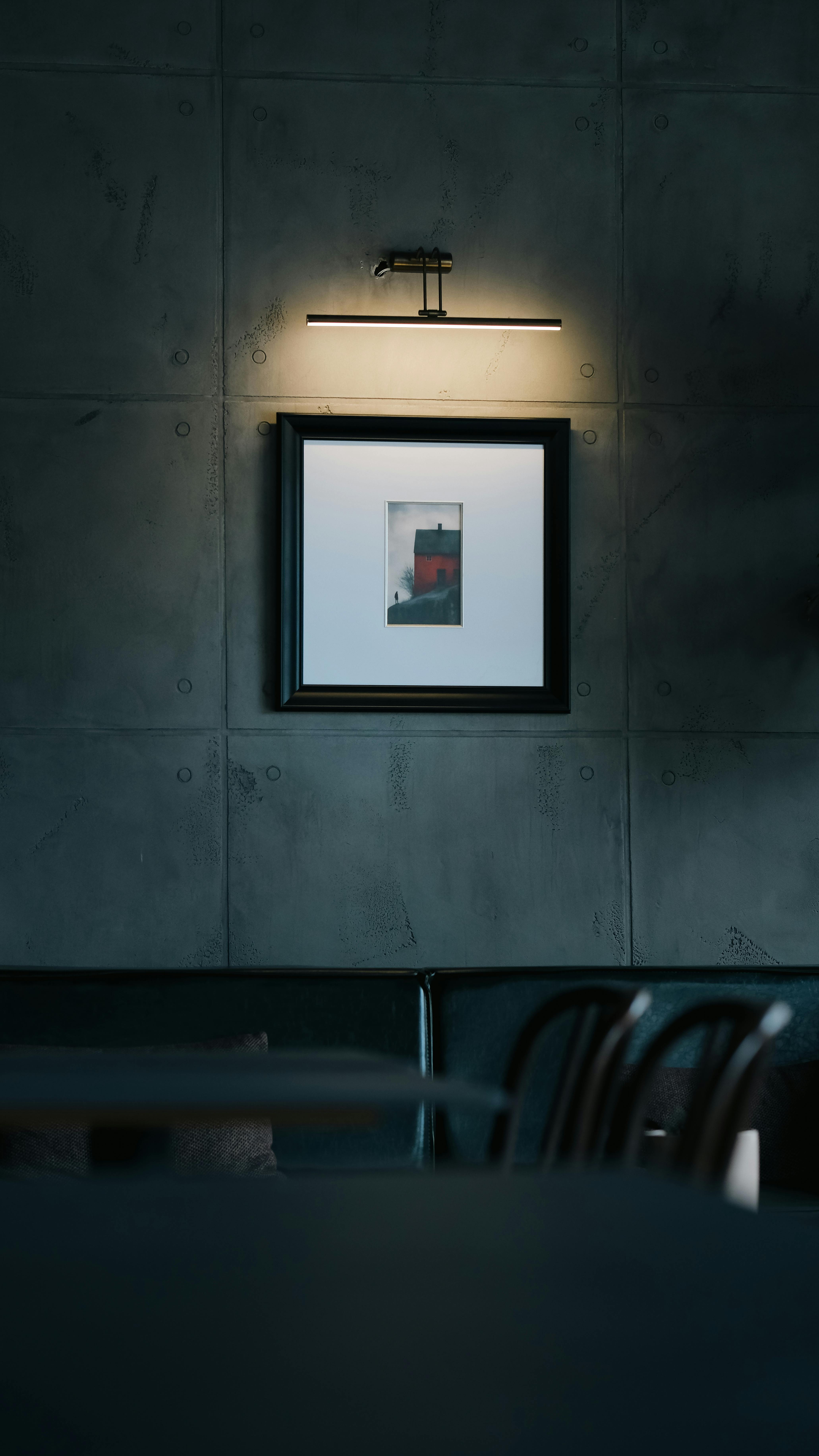 Gratis Et innrammet kunstverk opplyst på en betongvegg i et moderne innendørs miljø, som utstråler en minimalistisk og stemningsfull atmosfære. Arkivbilde