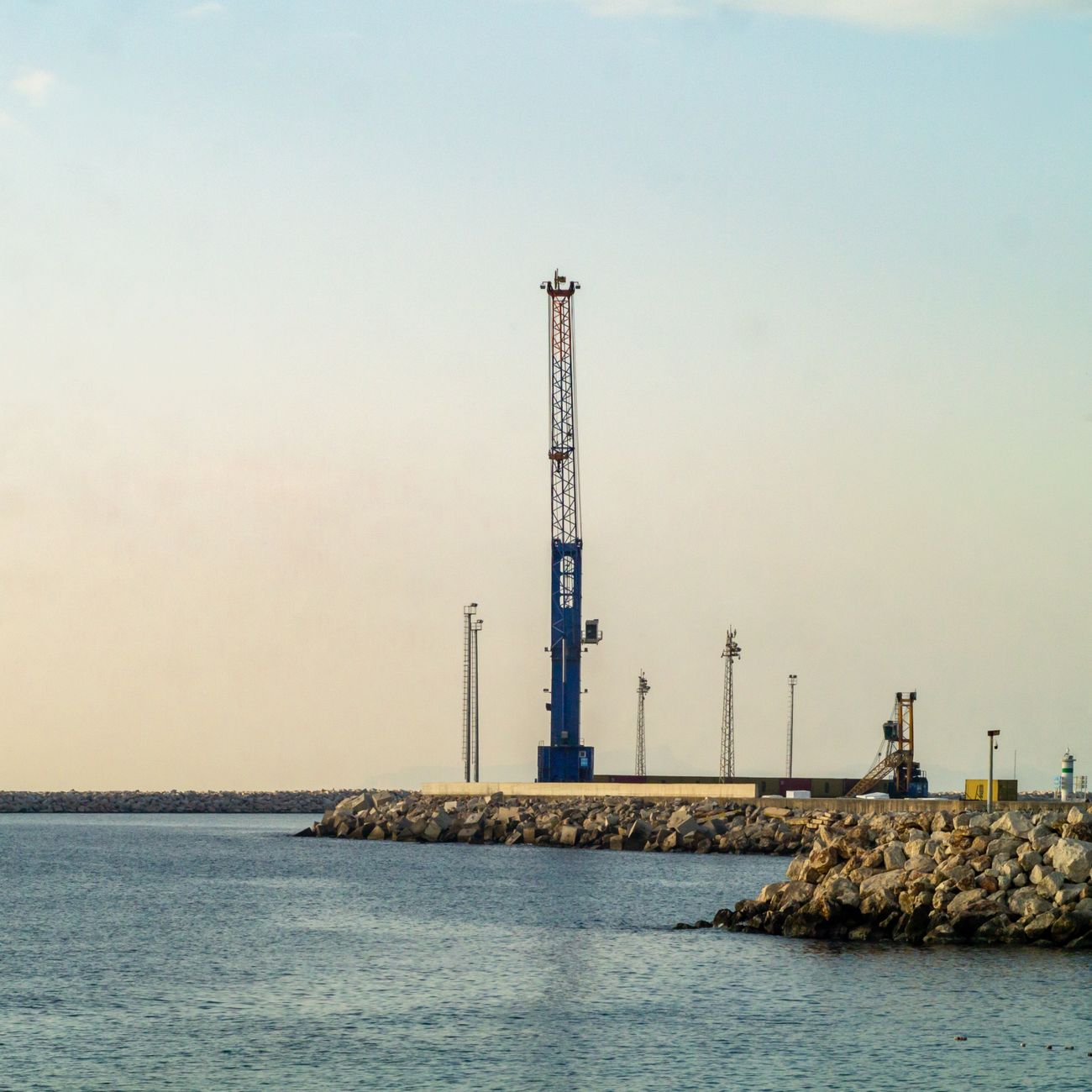 Industrial crane at a seaside pier during sunset, capturing a serene coastal landscape.