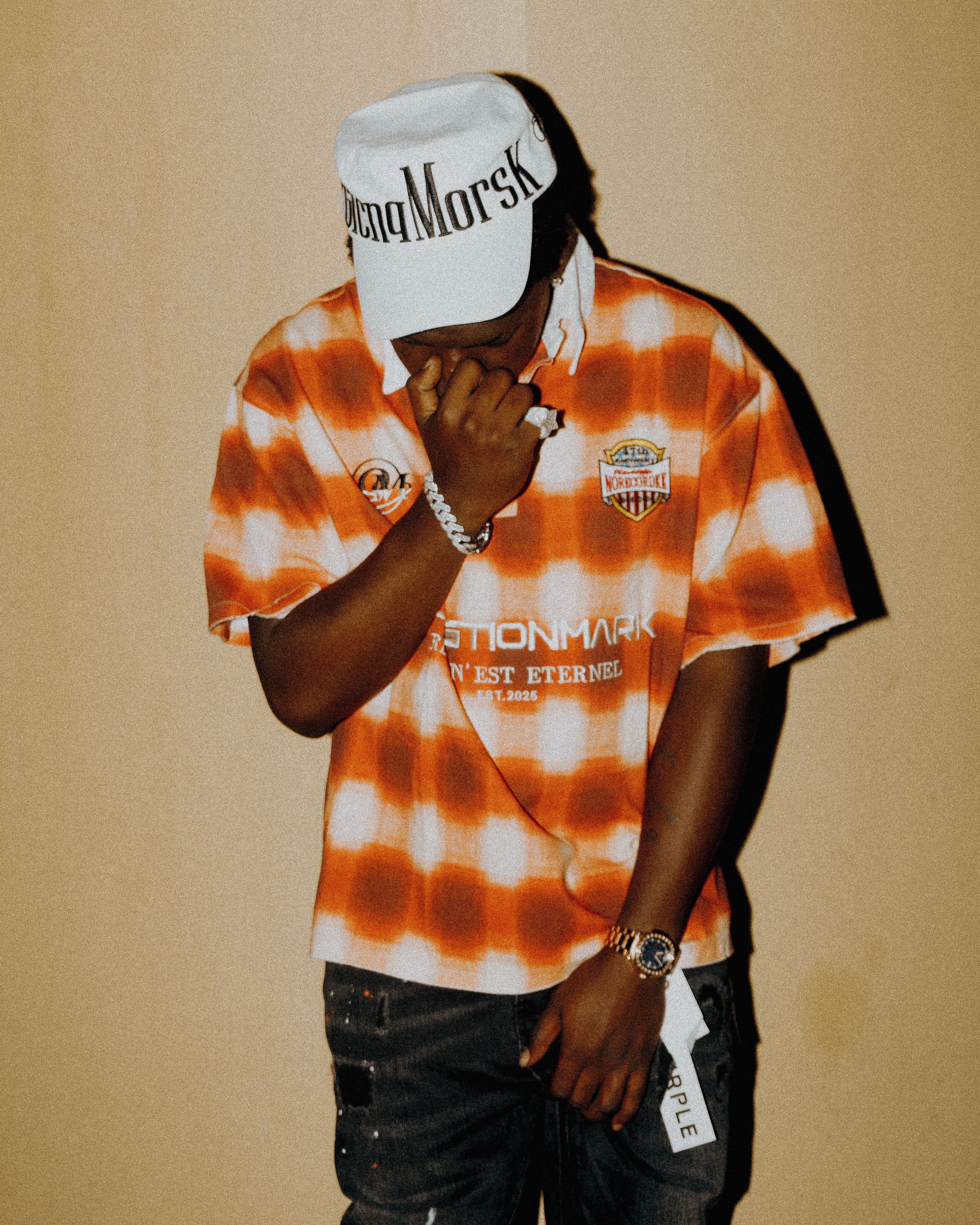 Young adult in urban streetwear fashion posing indoors against a neutral background.