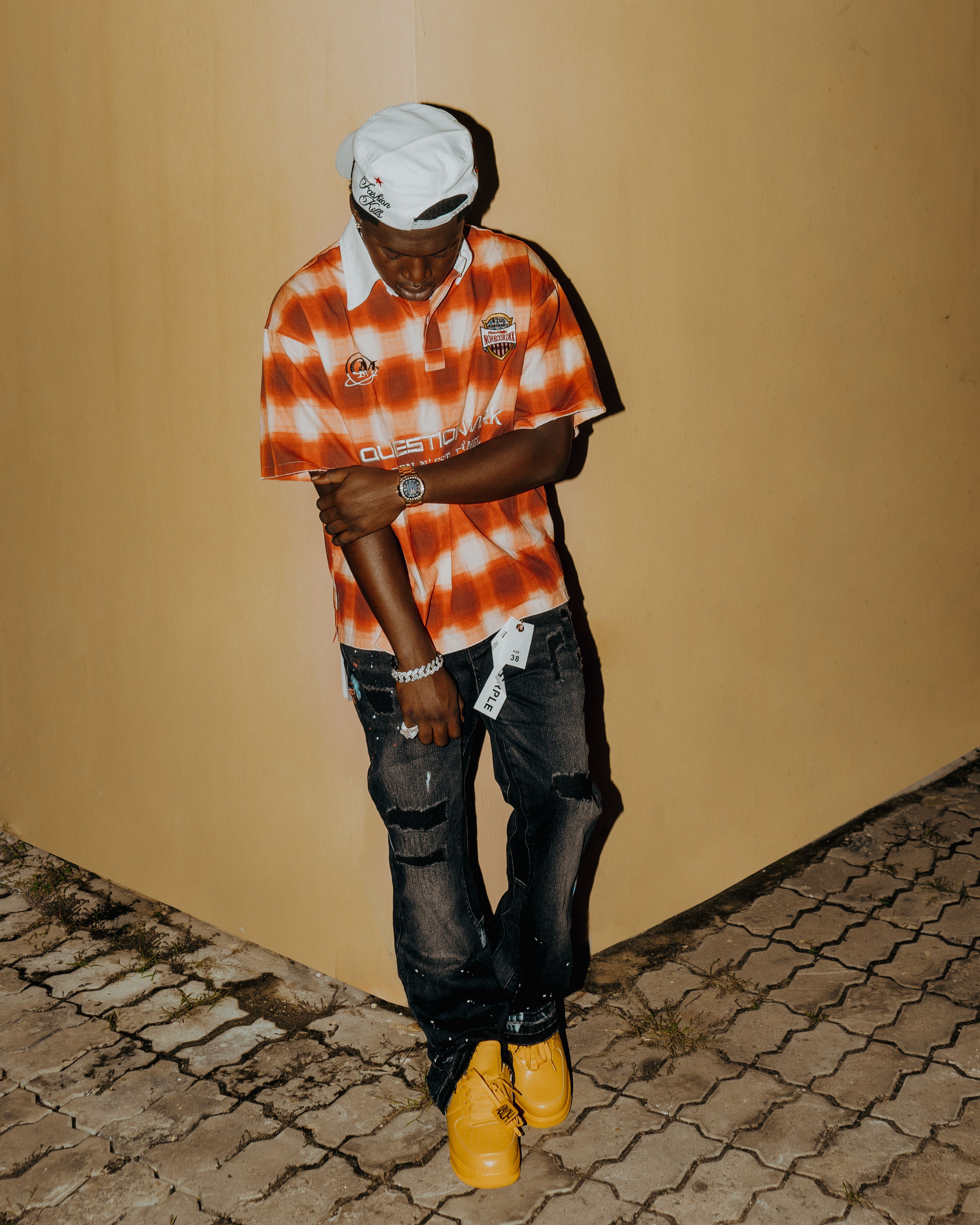 Young man in trendy fashion leaning against a wall at night.