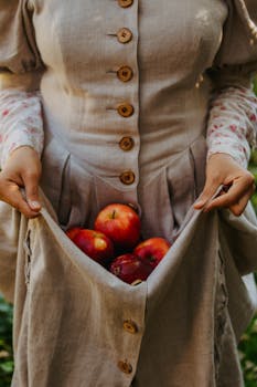 Close-up of a woman collecting red apples in her linen dress outdoors.