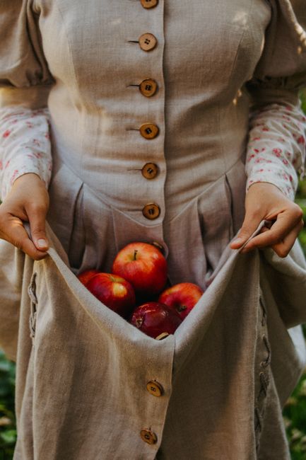 Close-up of a woman collecting red apples in her linen dress outdoors.