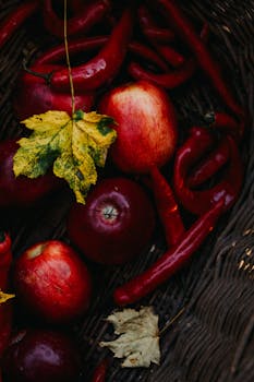 A basket filled with red apples, red peppers, and autumn leaves, evoking a rustic fall vibe.