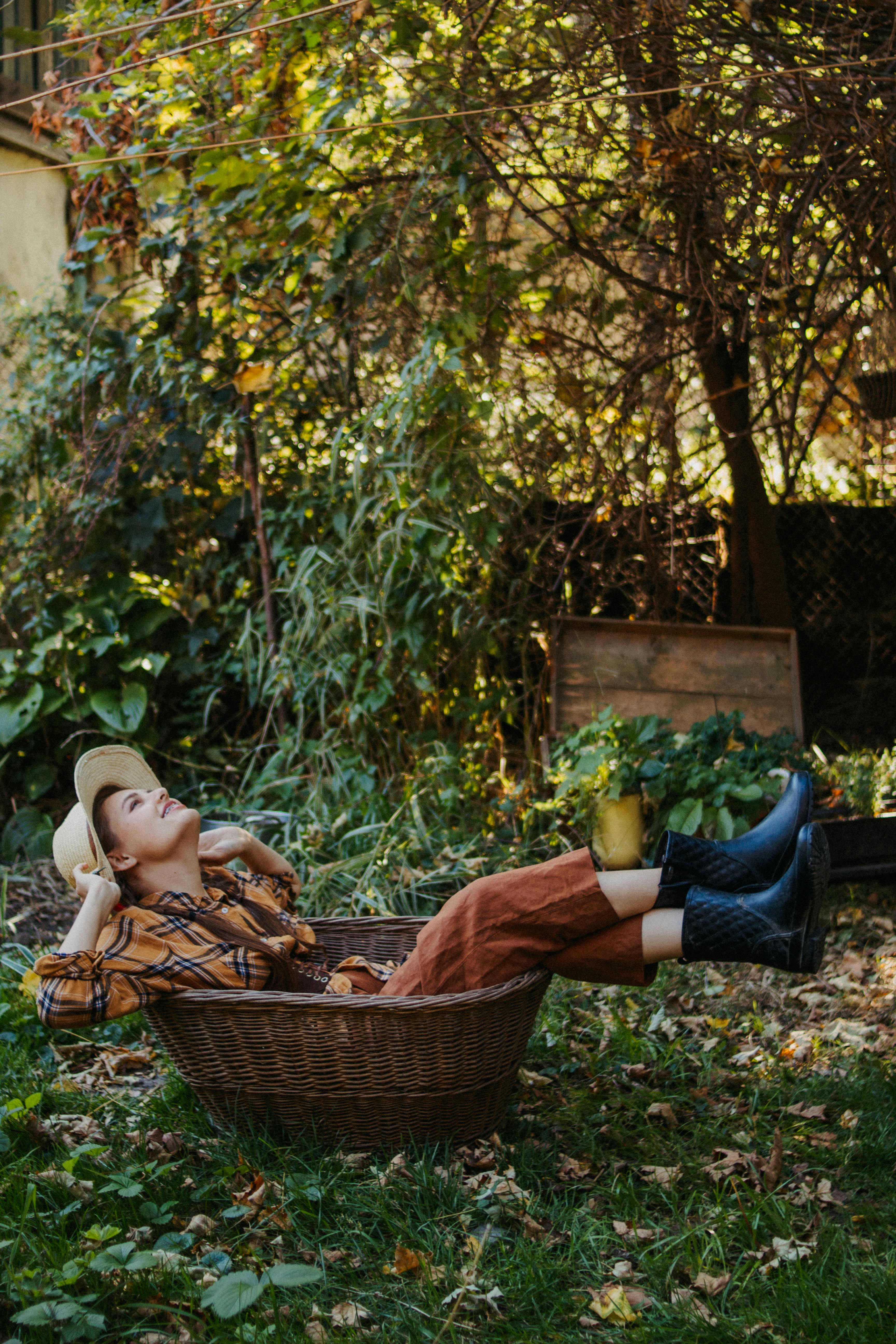 Woman in autumn clothing relaxing in a garden, lying in a basket with a serene expression.