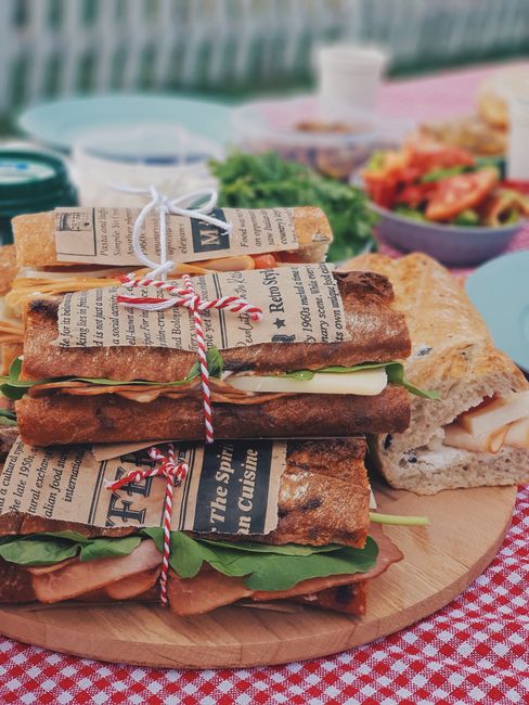 A rustic picnic setup with gourmet sandwiches and fresh salads outdoors.