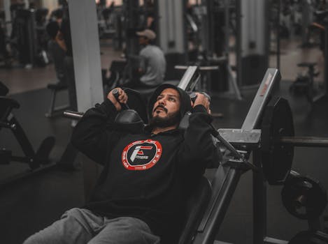 A man focuses intensely while lifting weights on a bench press machine in a modern gym.