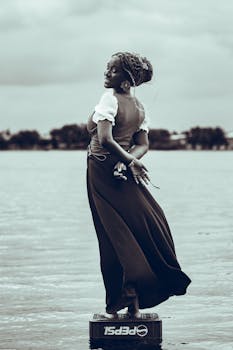 A woman in an elegant dress poses artistically by a serene lake in Accra, Ghana.