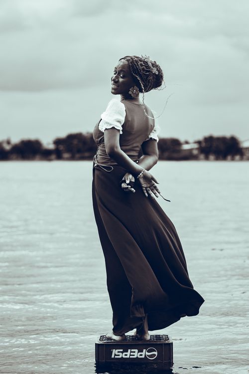 Free A woman in an elegant dress poses artistically by a serene lake in Accra, Ghana. Stock Photo