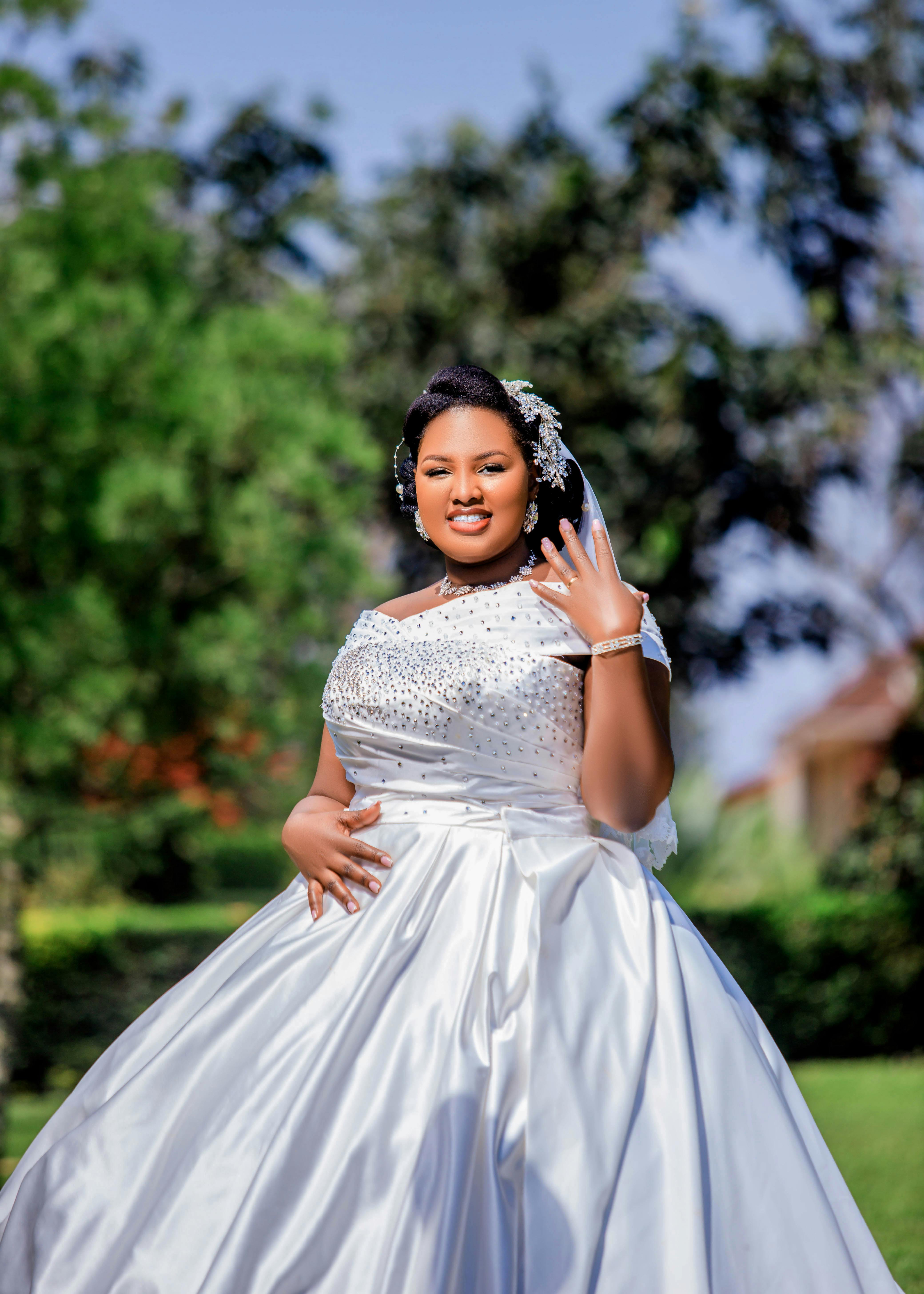 A beautiful bride in a white gown posing outdoors on a sunny day.