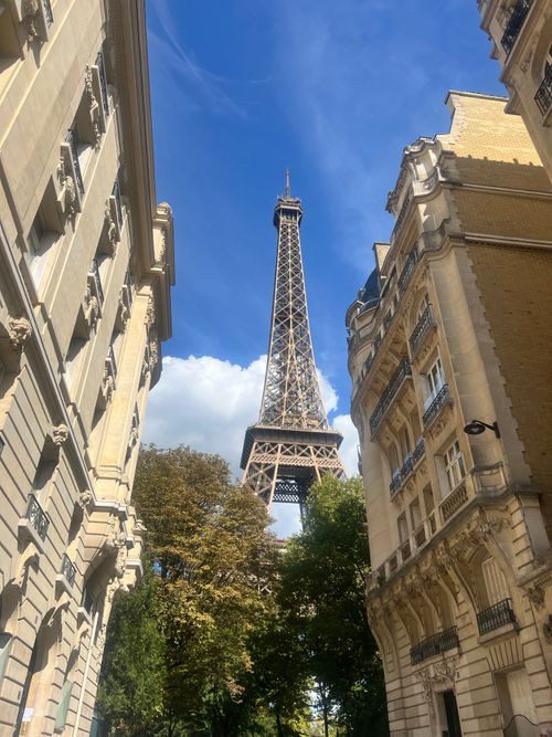 Free Iconic Eiffel Tower viewed through classic Parisian buildings under a bright blue sky. Stock Photo
