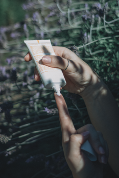 Close-up of hands with skincare cream against a lavender backdrop.