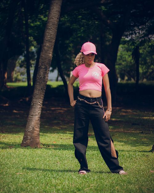 Free Confident woman in pink top and cap poses outdoors in a park setting. Stock Photo