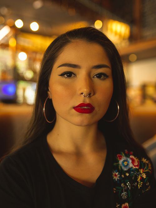 Free Portrait of a stylish woman with bold makeup and hoop earrings in a warm cafe setting. Stock Photo
