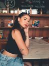 一位穿着休闲服装、纹着身的年轻女子，在咖啡桌前自信地摆着姿势