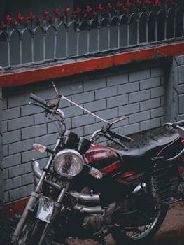 A classic motorcycle parked against a brick wall in Rangpur, Bangladesh, on a rainy day.