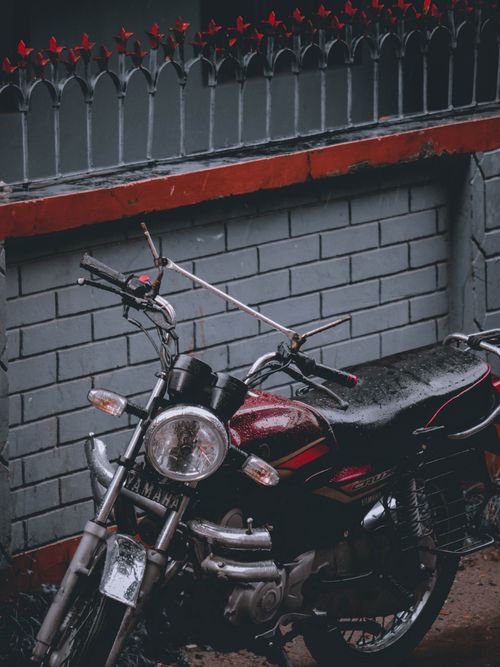 Free A classic motorcycle parked against a brick wall in Rangpur, Bangladesh, on a rainy day. Stock Photo