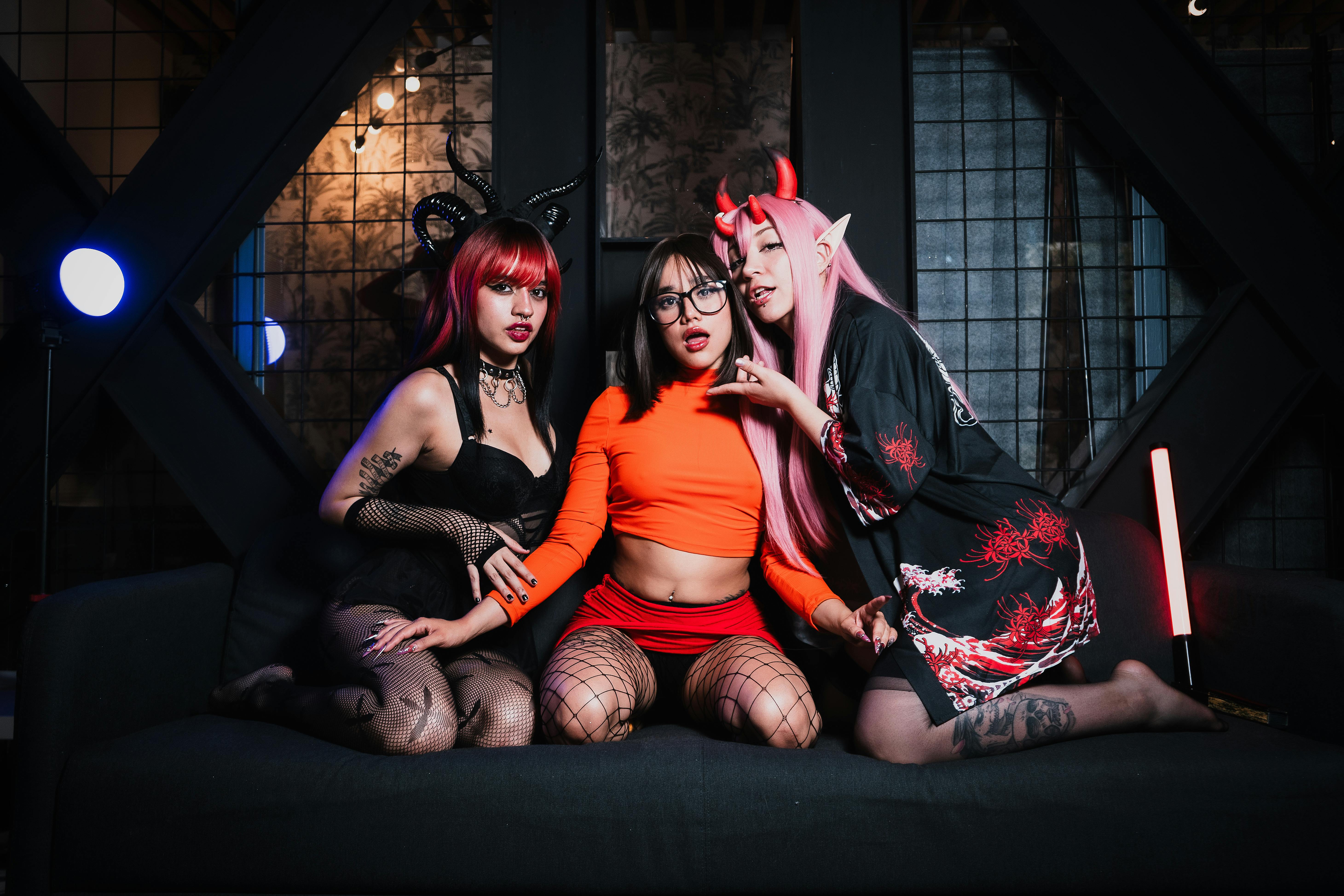 grátis Três mulheres fantasiadas de cosplay com luzes vibrantes em um ambiente interno, perfeito para conteúdo com tema de Halloween. Foto profissional