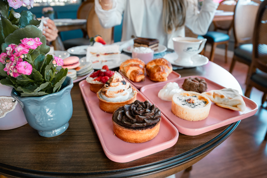 Assorted pastries and desserts on pink trays in a cozy café setting with blooming flowers.