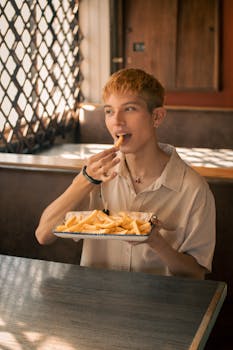 A young adult enjoying a plate of fries in a cozy, sunlit cafe with a charming ambiance.