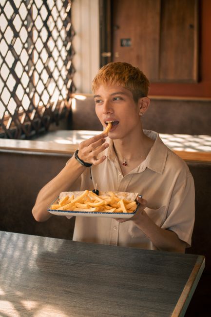 A young adult enjoying a plate of fries in a cozy, sunlit cafe with a charming ambiance.