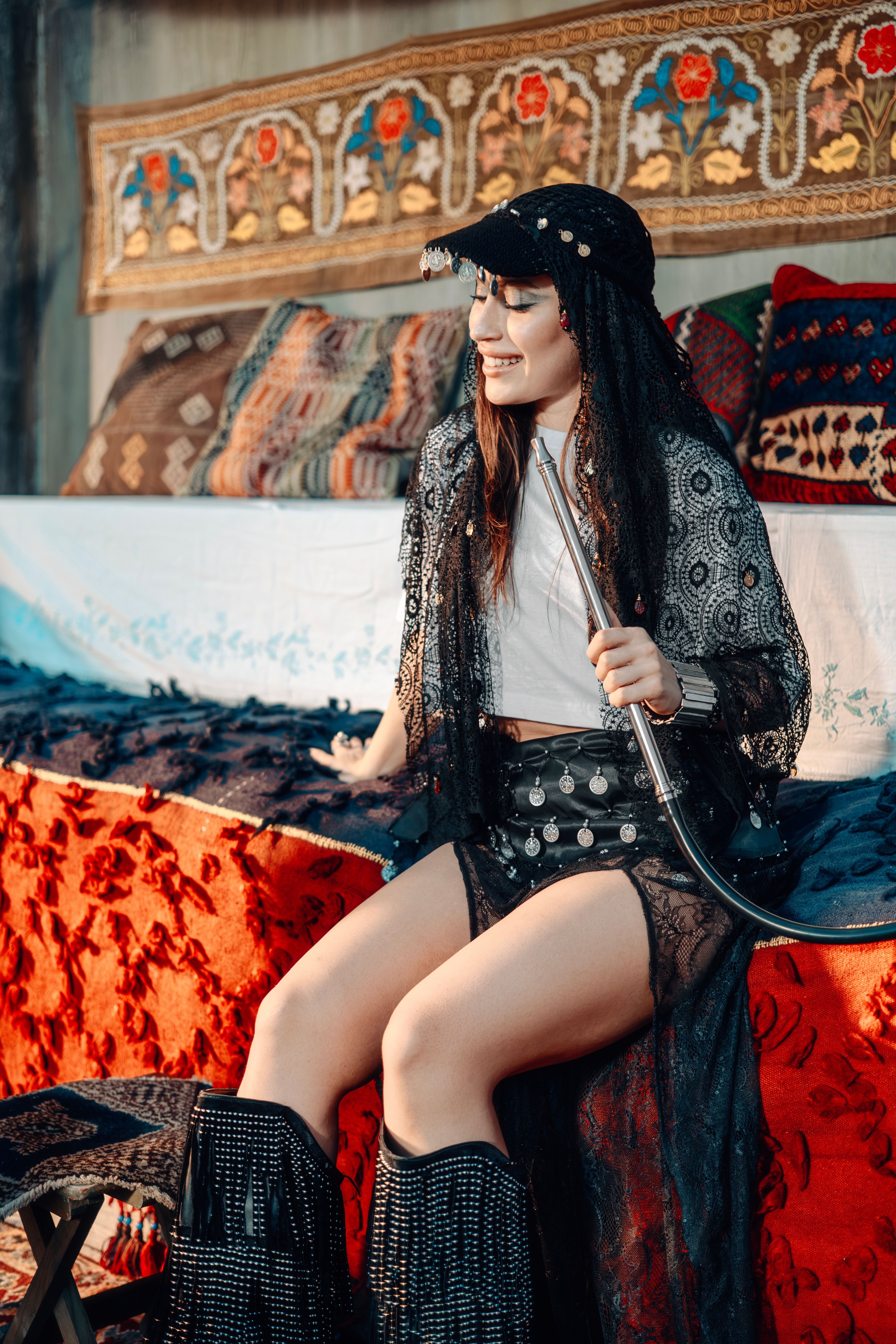 Beautiful young woman in traditional Middle Eastern attire enjoying a hookah pipe on a colorful couch.