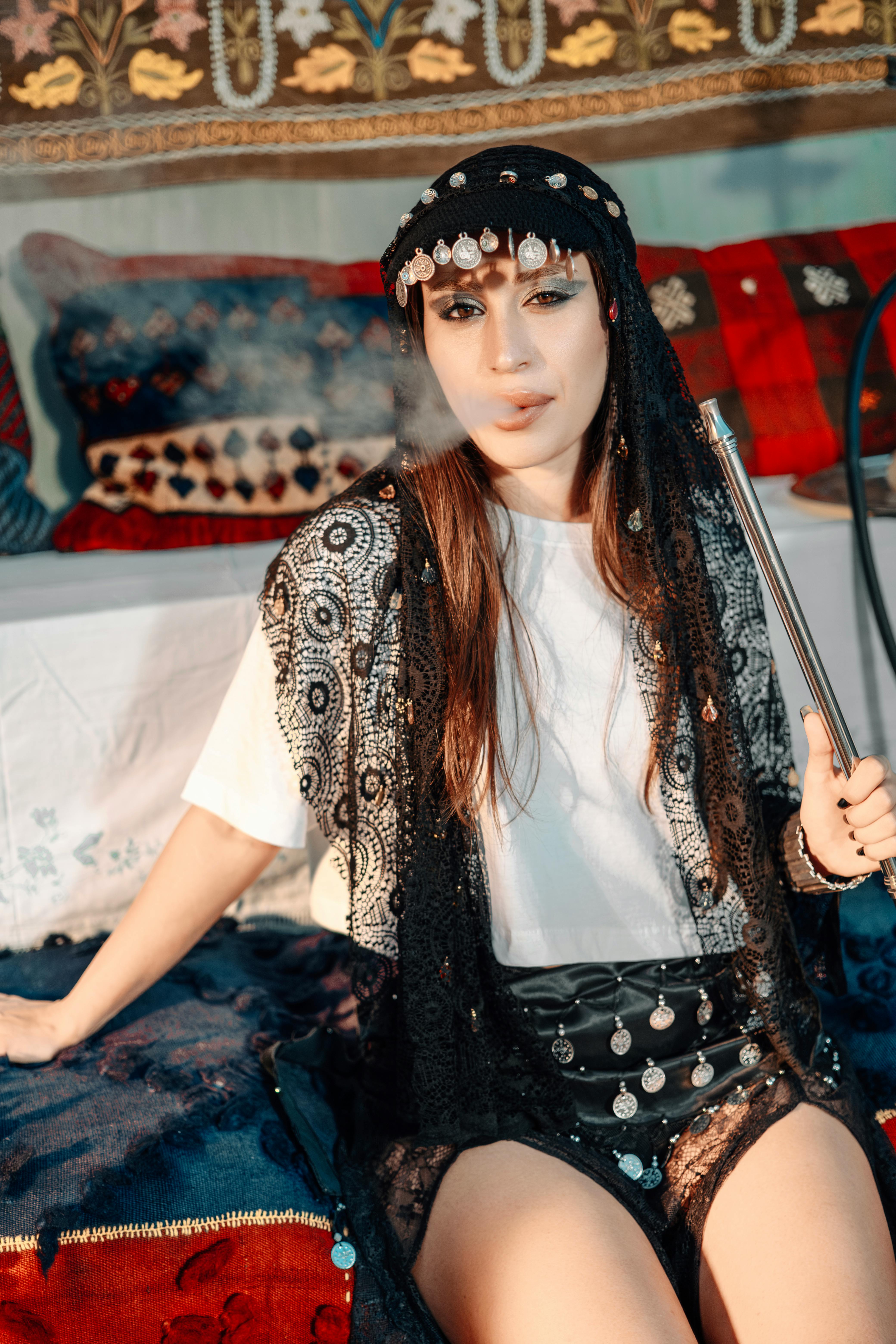 Young woman in ethnic attire enjoying a hookah in a cozy interior setting with vibrant textiles.