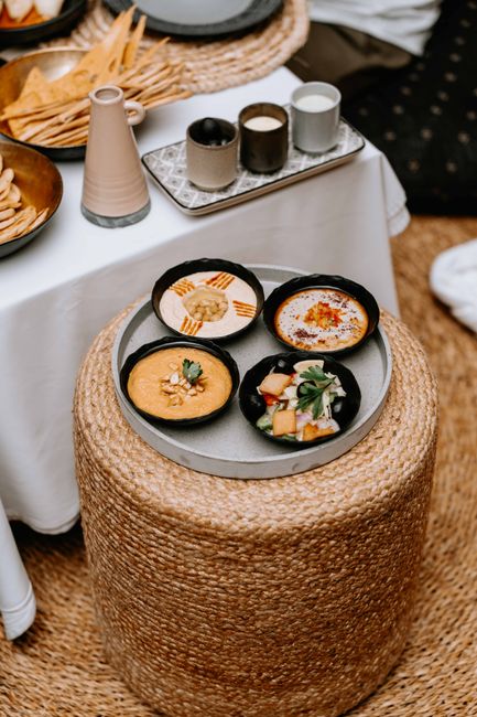An elegant display of Middle Eastern dips with fresh garnishes on a woven ottoman, perfect for a lavish meal.