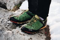 绿色登山鞋在岩石、雪地地形上的特写，非常适合户外冒险的视觉效果