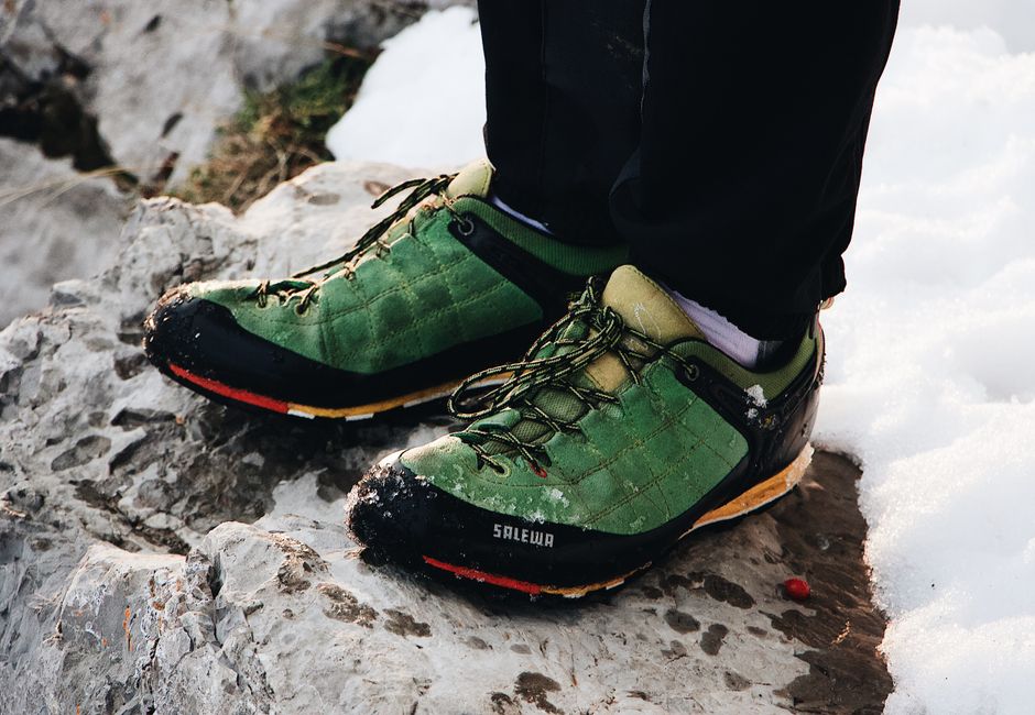 Close-up of green hiking shoes on rocky, snowy terrain, perfect for outdoor adventure visuals.