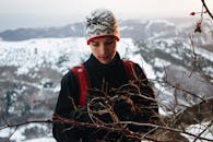 一名穿着冬装的年轻人在雪山背景下检查贫瘠树枝上的相机
