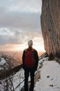 一位孤独的徒步旅行者站在白雪皑皑的山路上，凝视着美丽的日落