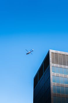 A helicopter flying over a modern building in Grand Rapids, Michigan, during a bright clear day.