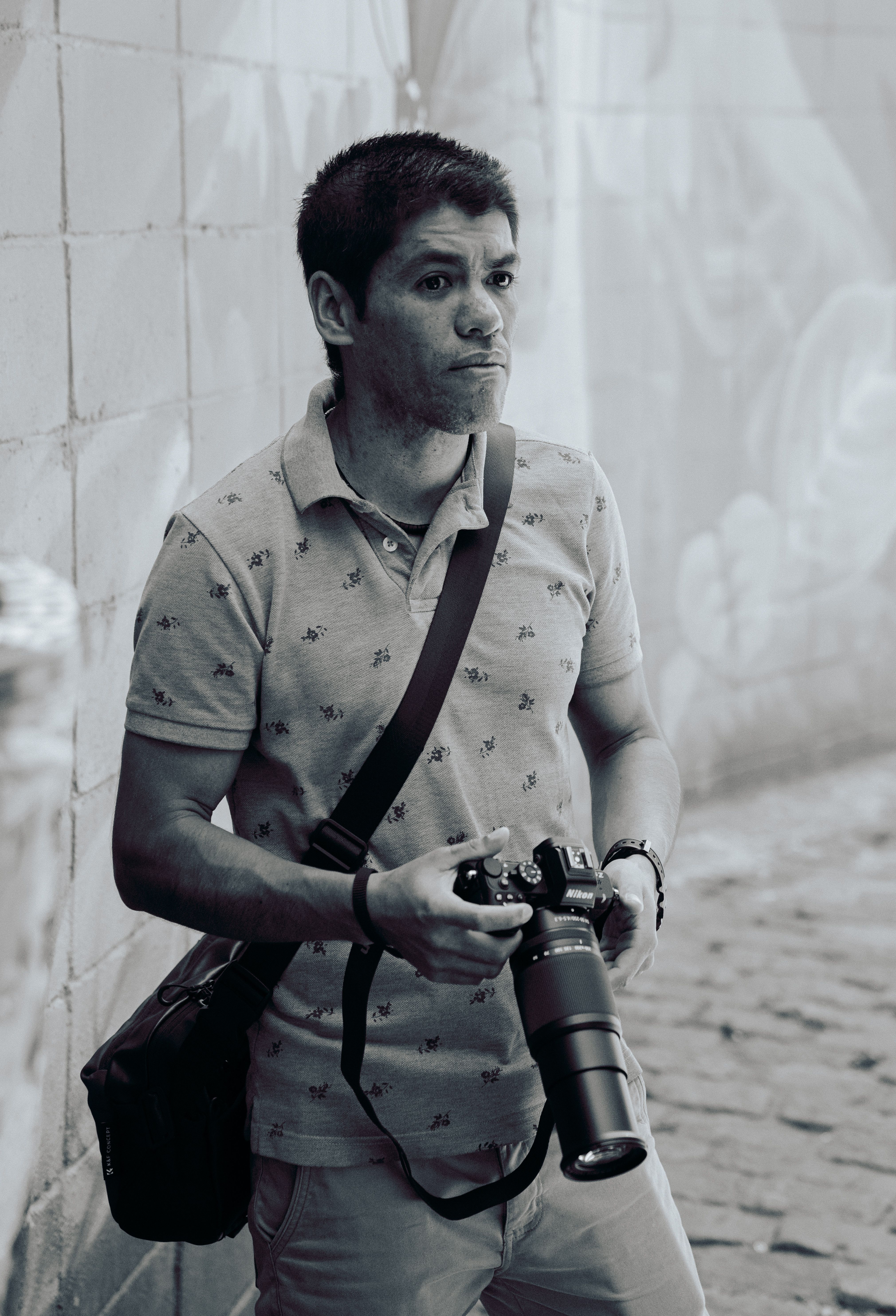 Black and white image of a male photographer holding a camera in a cobbled alley in São Paulo.