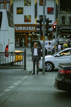 An older man stands at a bustling Istanbul crosswalk with traffic and storefronts in view.