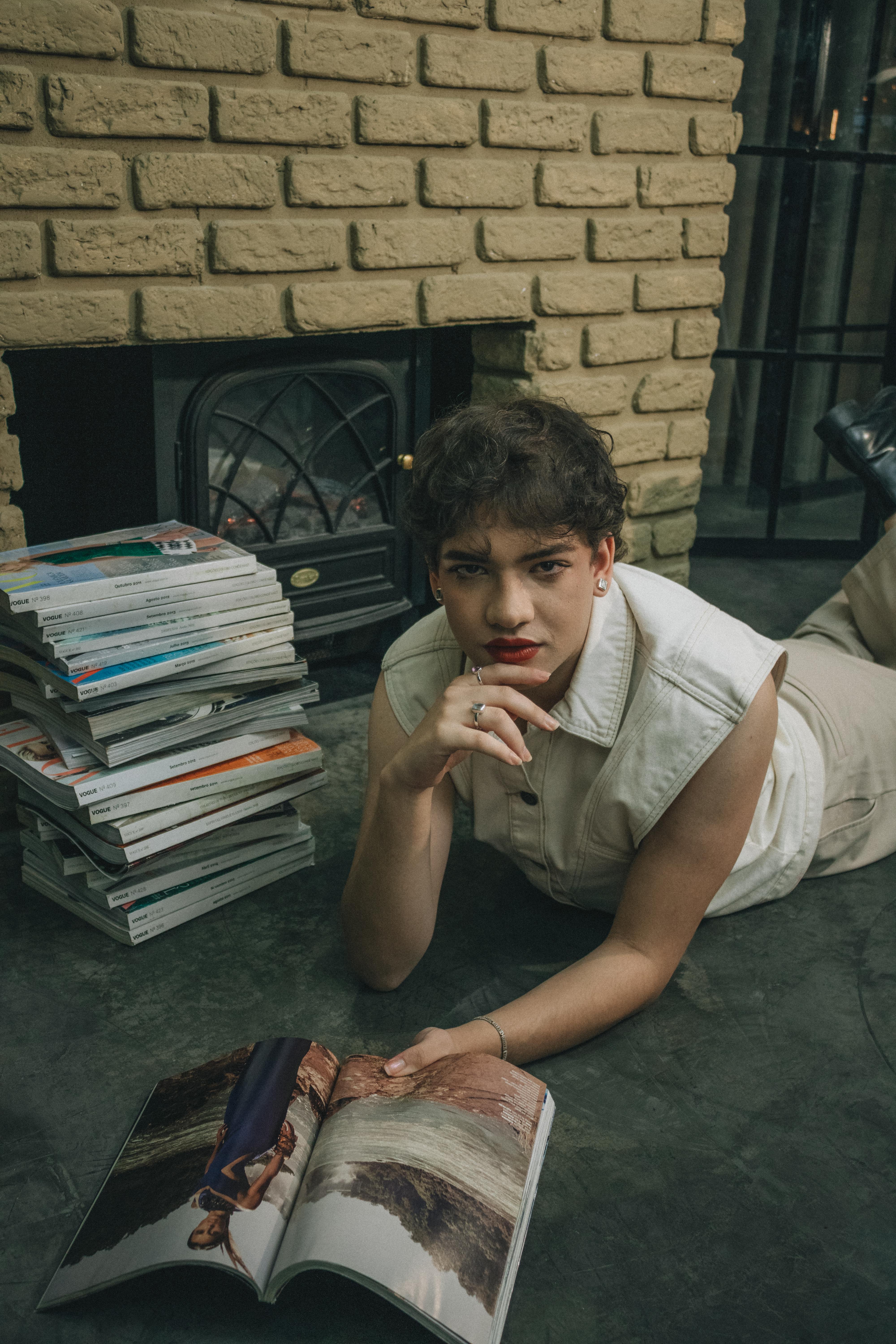 Person relaxing indoors, reading a magazine by a cozy brick fireplace.