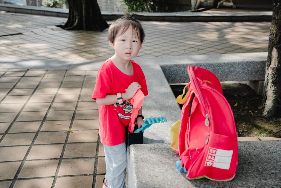 Kind mit großer roter Schultasche auf einem gepflasterten Platz