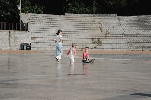 Free Three children enjoying outdoor playtime on a skateboard at a public square during daytime. Stock Photo