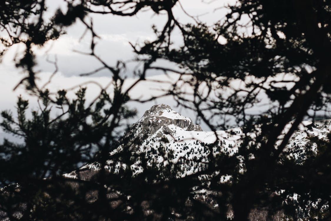 Long Shot Photo Of Snow Covered Mountain Peak Under Gray Cloudy Skies