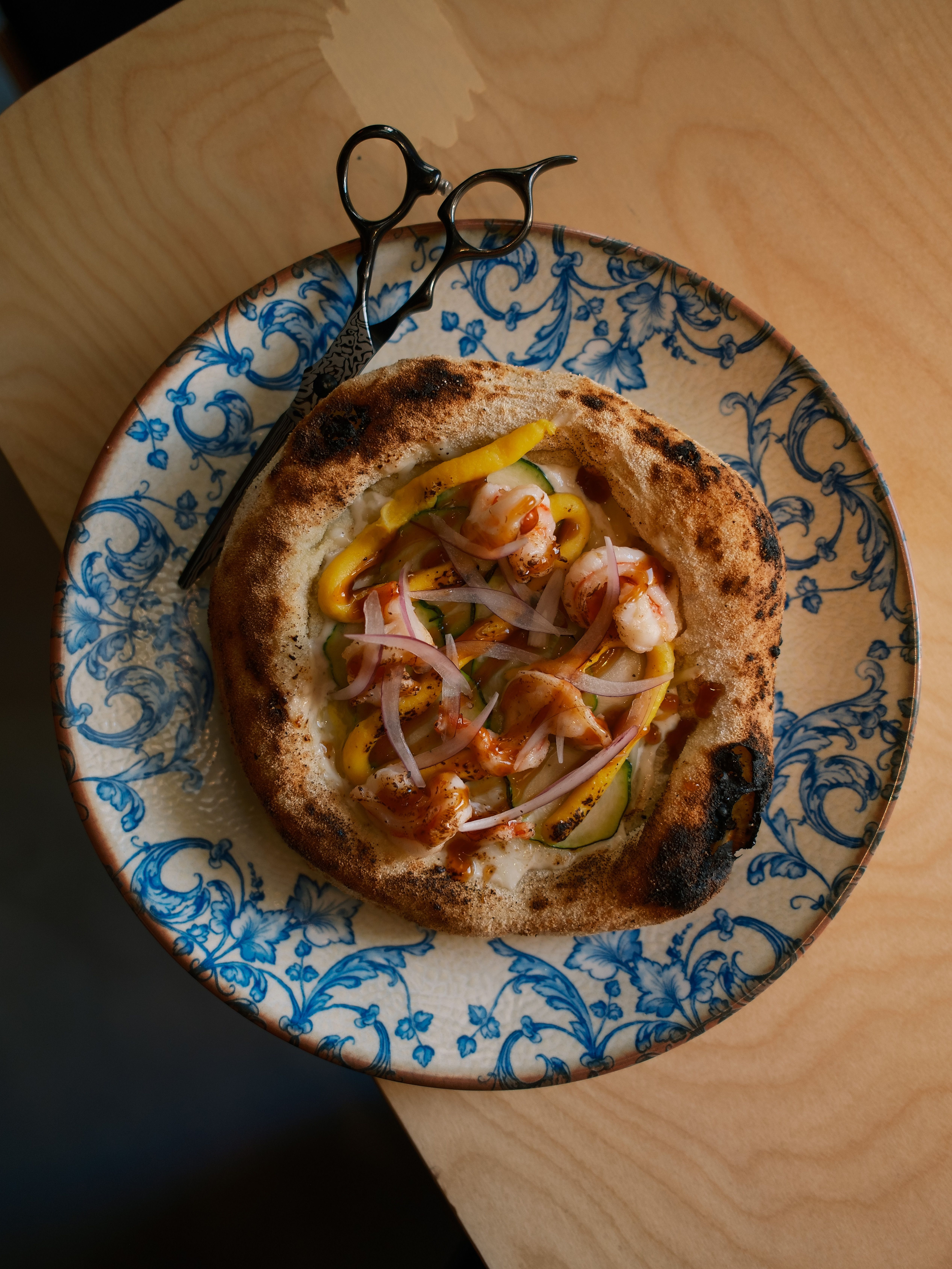 Gourmet flatbread pizza topped with shrimp and onions on a classic floral plate.