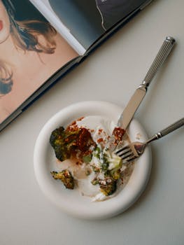 A styled flat lay of a broccoli plate with cutlery and a partially open magazine.