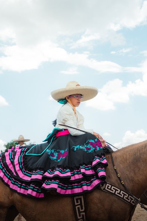 Free A woman in traditional charro attire rides a horse under a bright blue sky in Hidalgo, Mexico. Stock Photo